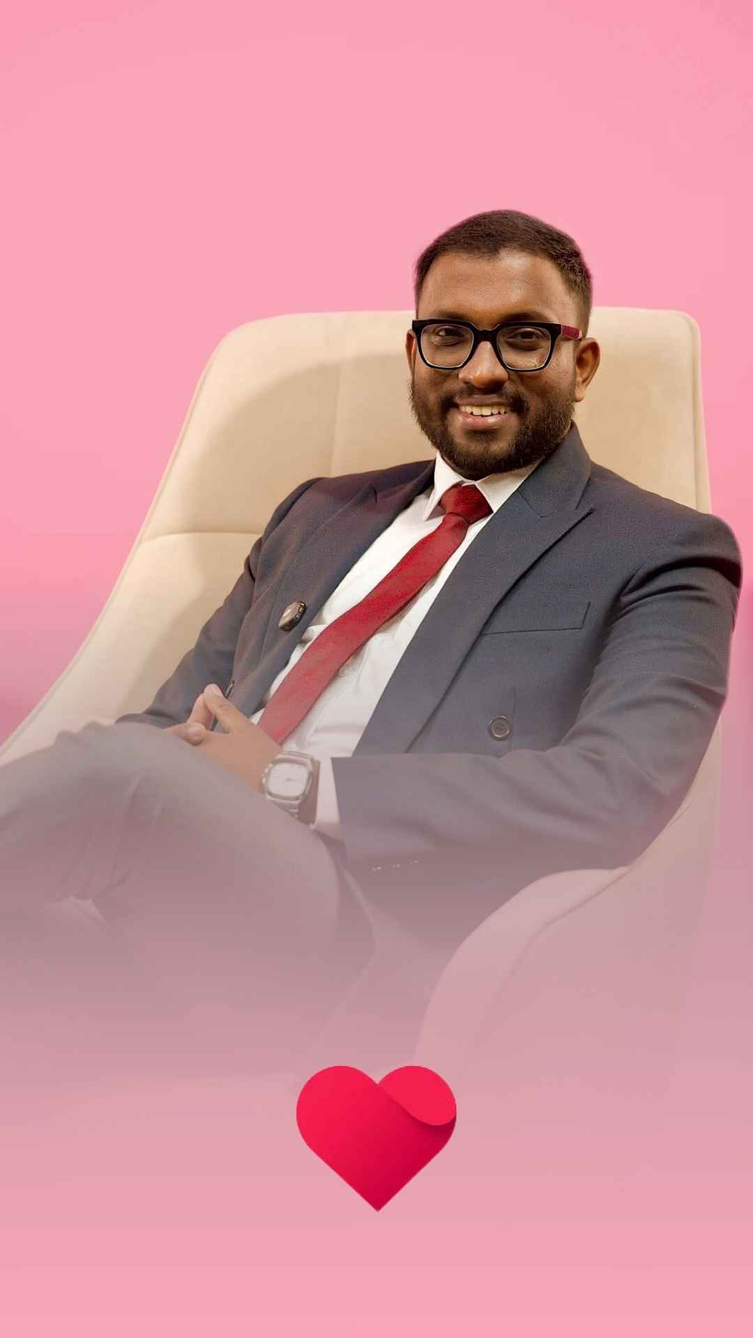 Mayantha presenting to camera in a dark suit against a pink set, for Invitation.lk
